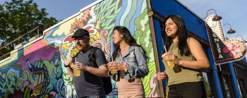 walking toward the sun, three people pass a colorful mural painted on the side of a building