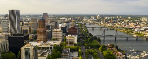 aerial view of downtown area with buildings and roadways, bridges crossing a river to a smaller set of buildings that expand into the distance