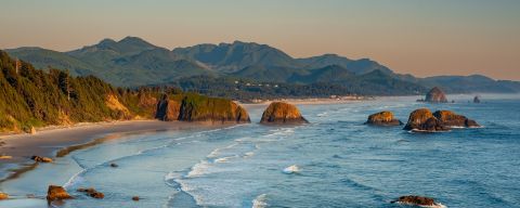 an aerial view of the Oregon Coast with the coast mountain range in the background, a sea of green