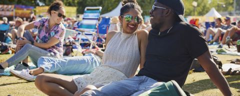 two people sit together in the sunshine in the middle of a crowd