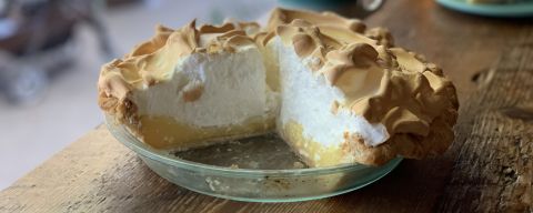 a tall lemon meringue pie with a couple of slices missing sitting in a glass pie dish