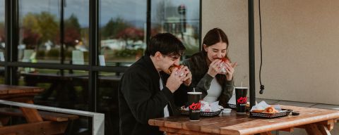A couple sits at a picnic table eating burgers.