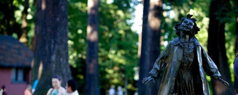 a bronze statue of a little girl with a fountain of water at her feet and people picnicking in the background