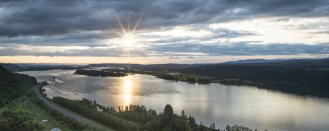 The sun breaks through clouds above a wide river