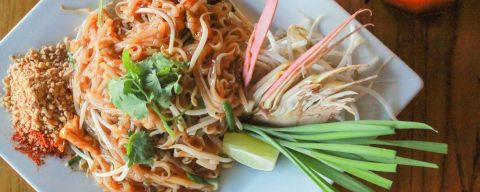 a closeup of a plate of thai food and thai iced tea