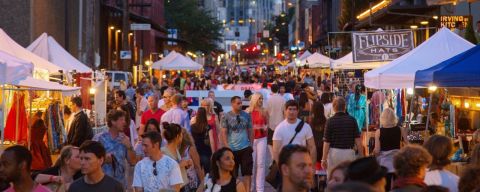 a twilight street filled with people browsing tents with items on display