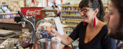 A woman spoons the whipped cream from the top of a milkshake at a pharmacy soda fountain