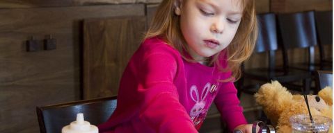 A young girl adds chocolate chips and blueberries to a pancake.