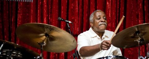 a man playing drums on stage in front of a red curtain