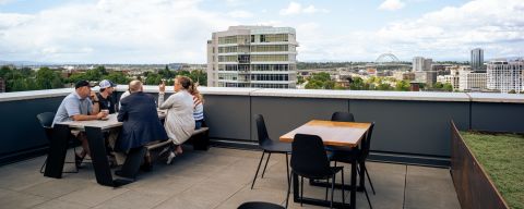 a group of people enjoy drinks on a rooftop bar patio overlooking the city