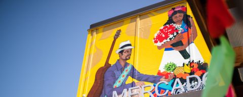 A sign reading \"Portland Mercado\" in front of a brightly painted mural showing a Latin American dancer and musician