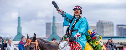 native american woman on colorfully decorated horse waves in parade