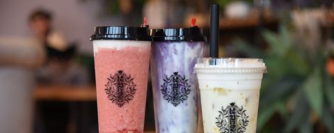 Three cups of flavored boba tea rest on small wooden table.