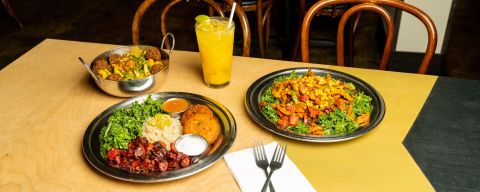 several plates of Indian food and an iced orange drink atop a wooden restaurant table
