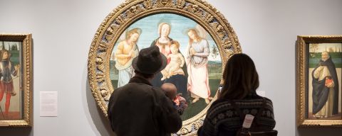 two people and a baby stand in front of a round oil classical painting of a religious scene at the Portland Art Museum