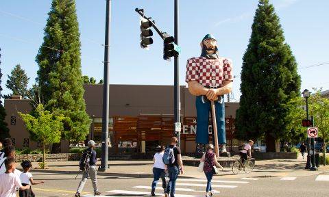 people cross the street in front of a 31-foot-tall (9.5 m) statue of Paul Bunyan