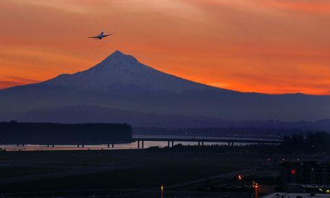 the silhouette of a plane against an orange sunset with Mount Hood in the background
