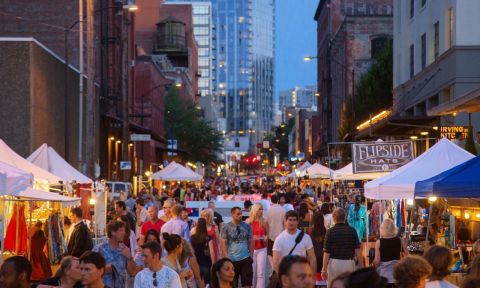 a twilight street filled with people browsing tents with items on display