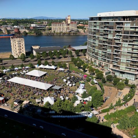 Aerial shot of an urban riverside park with festival tents and umbrellas