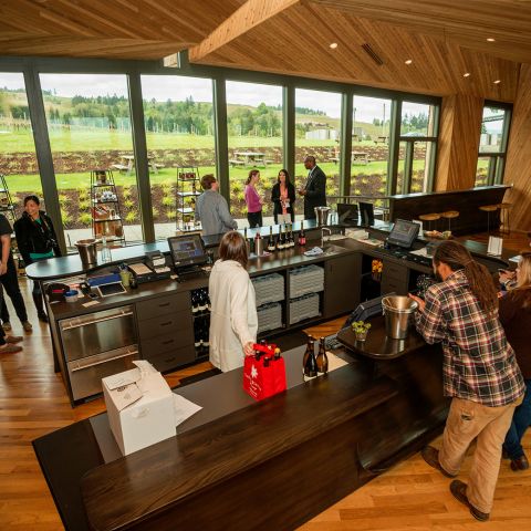 Patrons gather around a bar in a winery tasting room.
