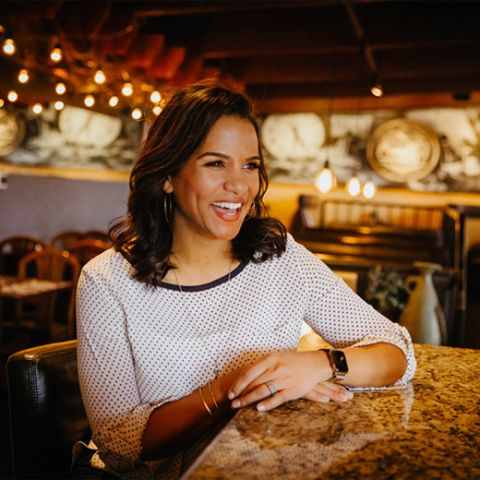 a smiling woman sits at a table in a restaurant
