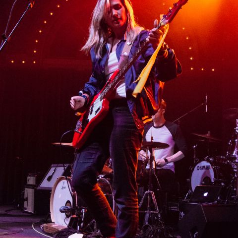 A bassist performs on stage in front of a drummer