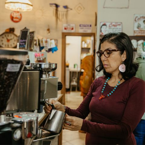 a woman steaming milk at an espresso machine