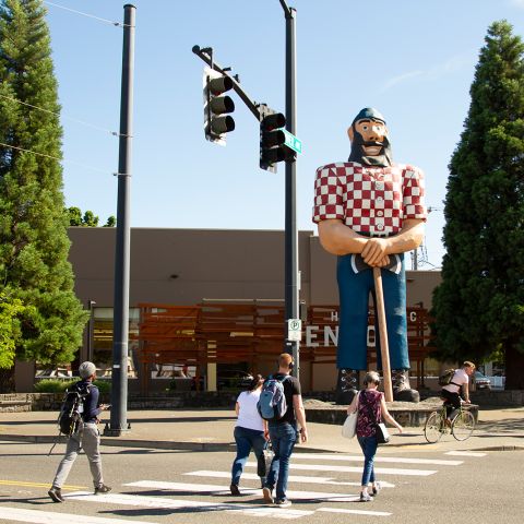 people cross the street in front of a 31-foot-tall (9.5 m) statue of Paul Bunyan