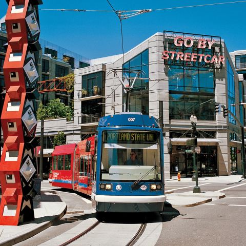 A streetcar passes by a large, red sculpture in front of a building with a neon sign reading, \"Go By Streetcar\"