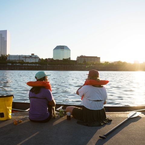 Two people sitting on a dock on the river alongside a kayak