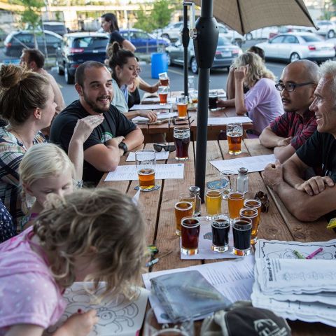 people of all ages around a picnic table covered with draft beers and coloring books