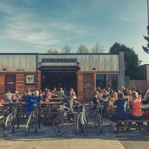 many people occupy a brewery\'s patio seating beneath a partly cloudy sky