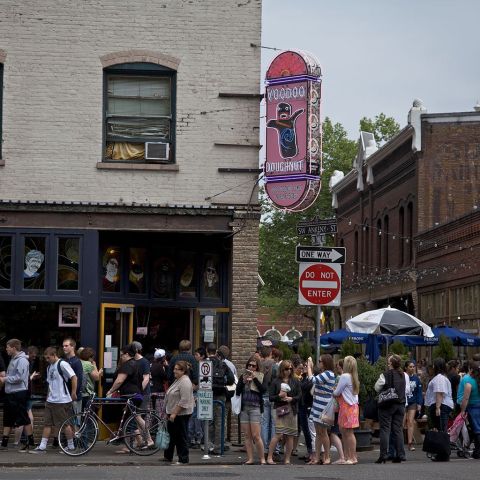 a long queue of people lined up outside a business, under a big pink sign