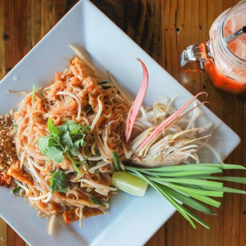 a close-up of a plate of Thai food and Thai iced tea