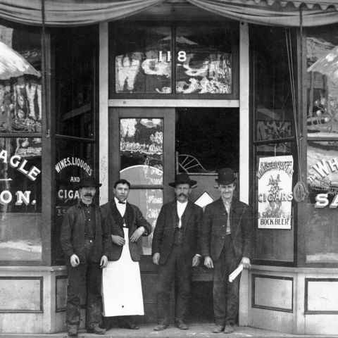 a black and white photo of three men standing in front of a saloon