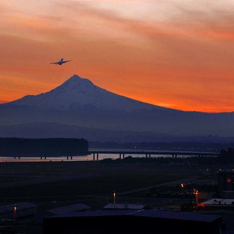 the silhouette of a plane against an orange sunset with Mount Hood in the background