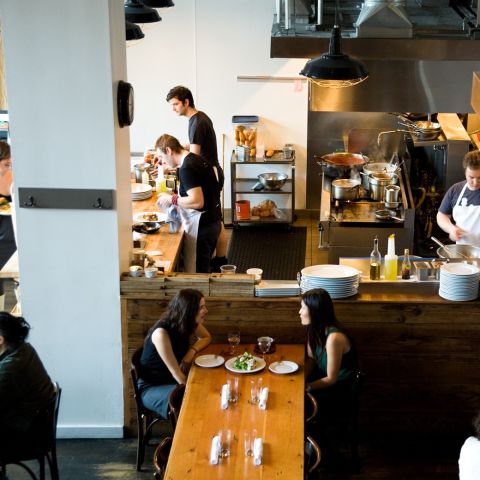 Diners enjoying food at Clyde Common with cooks prepping food in background.