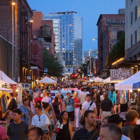 a twilight street filled with people browsing tents with items on display