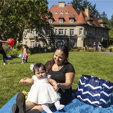 Woman and child sit on picnic blanket on the lawn outside of Pittock Mansion