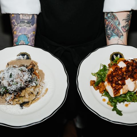 a person with tattooed forearms holds two plates of food