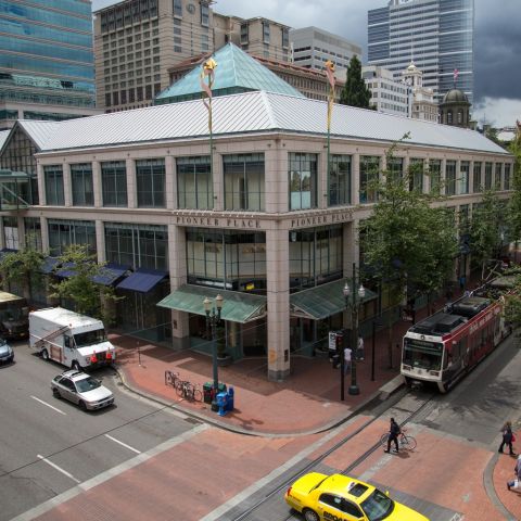 the exterior of a large urban shopping mall with vehicles and a light rail train out front