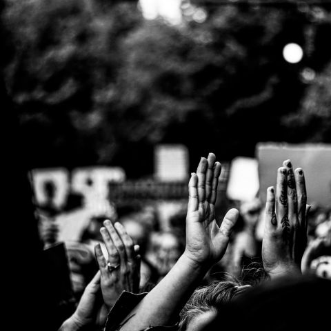 black and white image of hands raised within a crowd of protesters