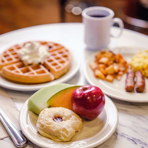 table with traditional breakfast foods, waffle, home fries, sausages, scrambled eggs and fruit with a pastry