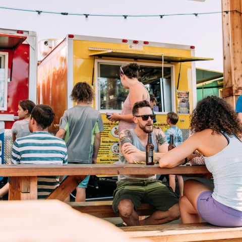 people sit at picnic tables in front of food carts