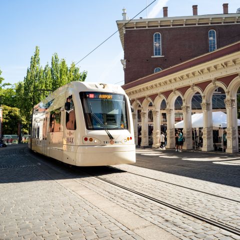 a light rail train on a cobblestone road passes the historic Saturday Market entry arches