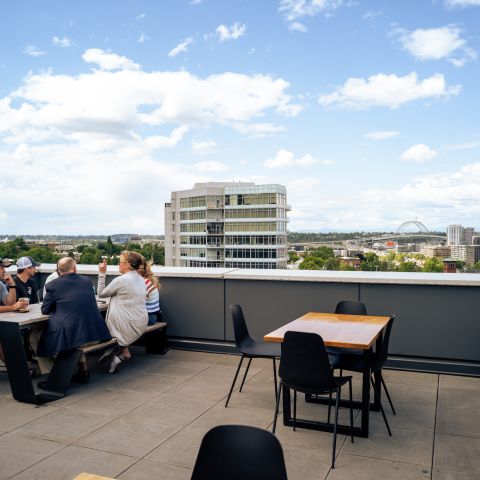 a group of people enjoy drinks on a rooftop bar patio overlooking the city