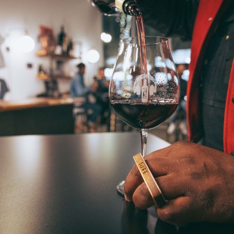 man with a gold finger ring holds a wine glass stem and pours a drink