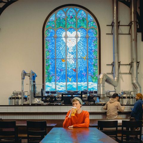 a person sips a beer in front of a stained glass window