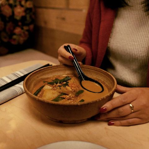 A person sitting at a table holds a ramen spoon in a bowl