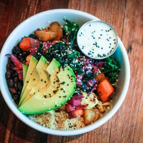 a bowl of brightly colored vegetables with avocado slices on top and a dressing on the side